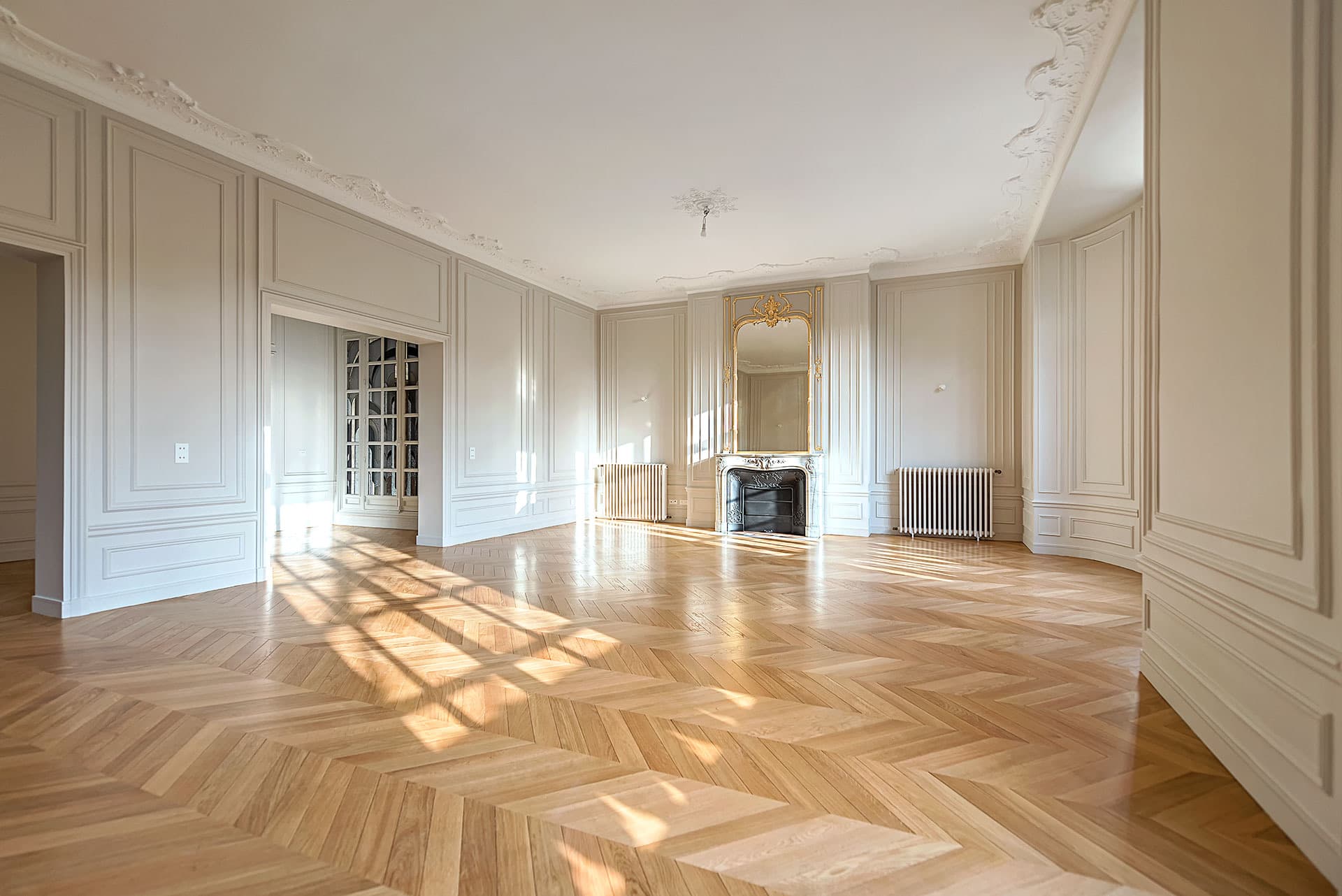 Grand salon rénové avec moulures, trumeau doré et parquet à chevrons